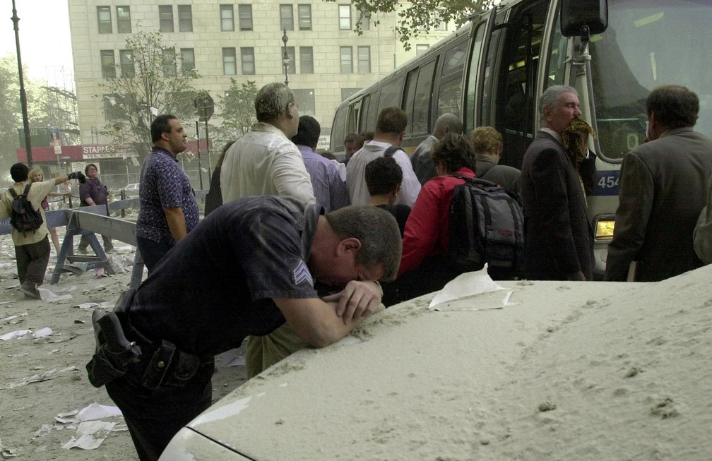 Exausto, um policial apoia a cabeça na traseira de um carro para descansar após a queda das torres do World Trade Center em 11 de setembro de 2001 - Foto: Stan Honda/AFP/Arquivo