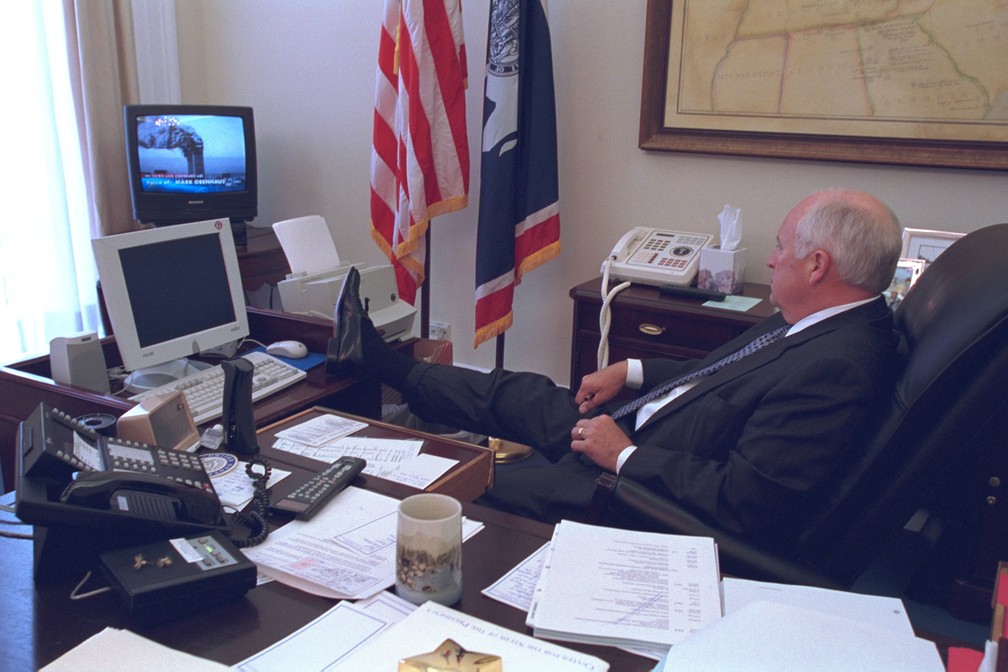 Com um pé apoiado sobre sua mesa em Washington, o então vice-presidente dos EUA, Dick Cheney, assiste à TV mostrando as torres do World Trade Center em chamas após os ataques aéreos do 11 de Setembro. A foto foi divulgada pelo governo dos EUA quase 14 anos depois, em julho de 2015 - Foto: Arquivo Nacional dos EUA via Reuters/Arquivo