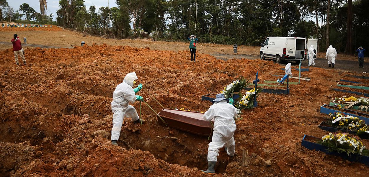 Coveiros vestindo roupas de proteção se preparam para enterrar no cemitério Parque Taruma, em Manaus.