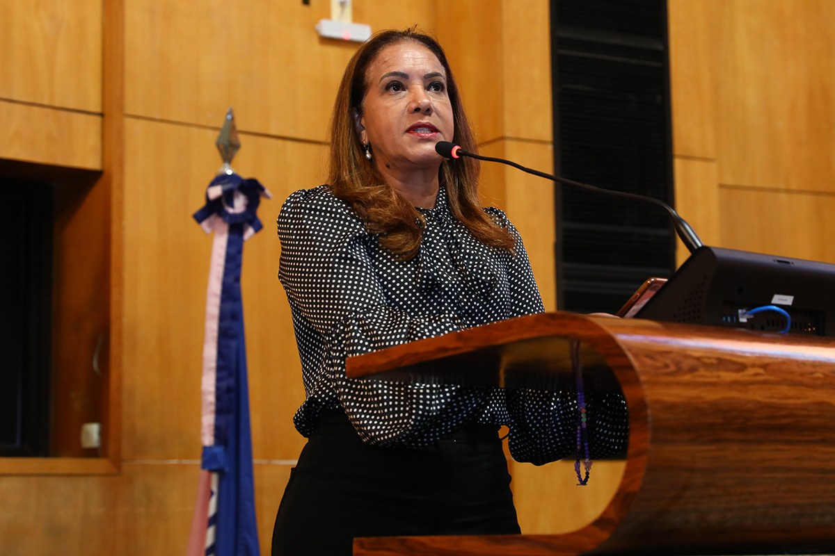 Janete de blusa preta com bolinhas brancas, ao microfone, na tribuna do plenário