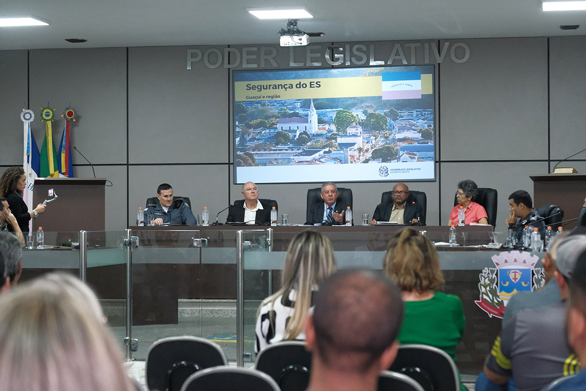 Pessoas sentadas e de costas em sala de reunião 